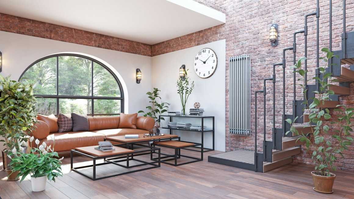 A cozy living room featuring a brown leather sofa, wooden coffee tables, and modern decor, with a large window allowing natural light, a stylish radiator on the wall, and a staircase leading to another level.