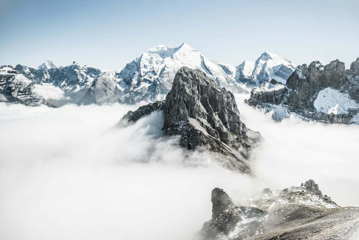 A scenic view of snow-capped mountains emerging from a blanket of clouds under a clear blue sky.